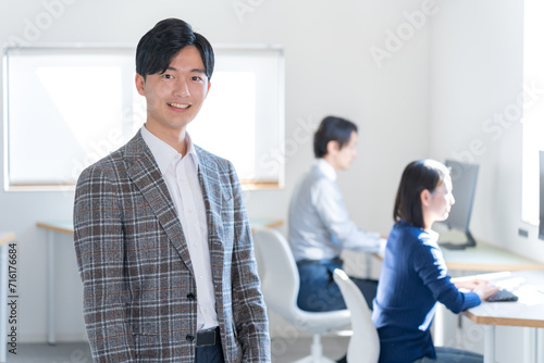 オフィスにいるカメラ目線のジャケットを着た若い日本人男性 photo