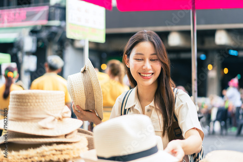Young Asian woman traveler tourist shopping for a hat and walking at outdoor market in Bangkok in Thailand. People traveling, summer vacation and tourism