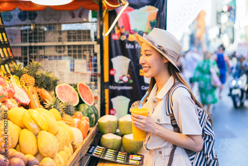 Young Asian woman traveler tourist buying a freshly made juice and walking at outdoor market in Bangkok in Thailand. People traveling, summer vacation and tourism
