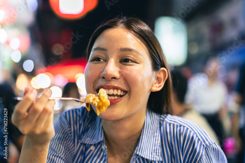 Young Asian woman traveler tourist eating Thai street food in China town night market in Bangkok in Thailand - people traveling enjoying food culture concept
