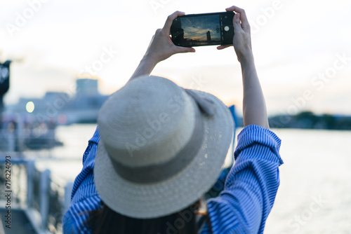 Traveler asian young woman using smart phone camera to take photo, selfie at riverside of Chaopraya River in Bangkok. Backpacker travel on holiday trip or vacation concept