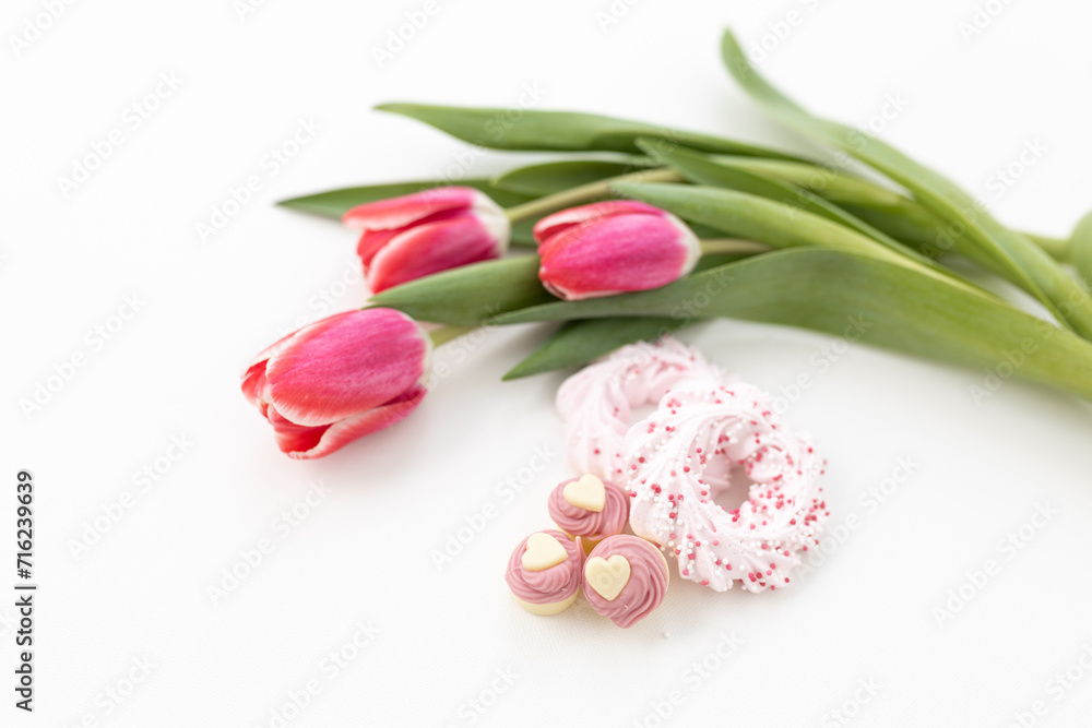 Fototapeta premium Pink tulips and heart-shaped pastries and candies on a white canvas close-up. Background for Valentine's Day, Easter. Gift for Women's Day, March 8th. Mockup