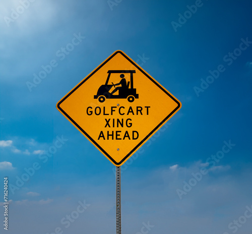 Yellow Golf Cart Crossing sign with black letters against a blue sky with clouds