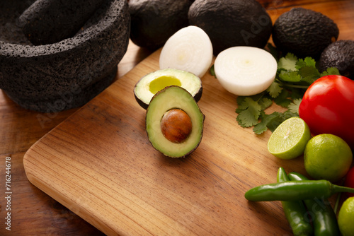 Basic ingredients to prepare avocado dip known as guacamole made in a volcanic stone molcajete, a very popular avocado-based sauce. Traditional recipe of Mexican cuisine.