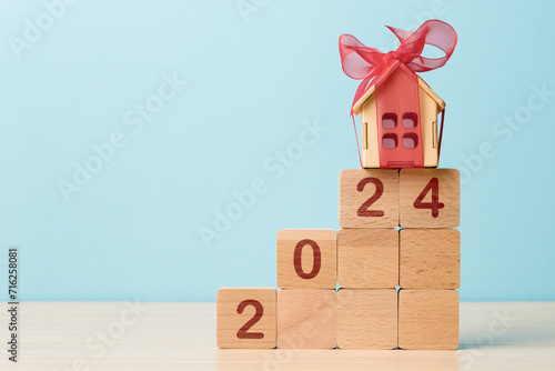 Small house gift with red bow on wooden blocks displaying 2024, symbolizing a new real estate or home purchasing in coming year