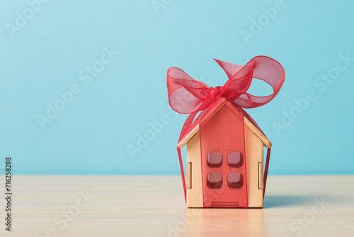 Small house gift with red bow over blue background with copy space. Concept of real estate gift