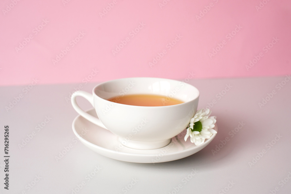 White set cup and plate with green tea stand on a pink background with white chamomile flowers White set cup and plate with green tea stand on a pink background with white chamomile flowers