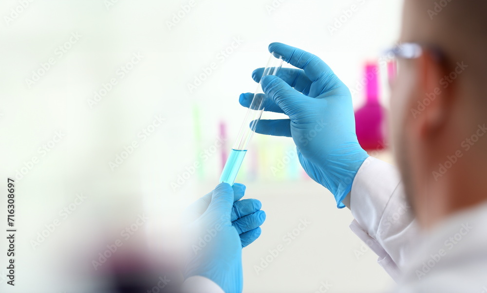 A male chemist holds test tube of glass in his hand overflows a liquid solution of potassium permanganate conducts an analysis reaction takes various versions of reagents using chemical manufacturing. A male chemist holds test tube of glass in his hand overflows a liquid solution of potassium permanganate conducts an analysis reaction takes various versions of reagents using chemical manufacturing.