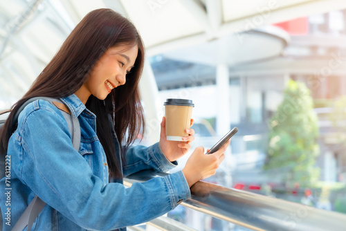 Young asian woman using mobile in city. Happy female tourist wearing jeans jacket and holding smartphone at public photo