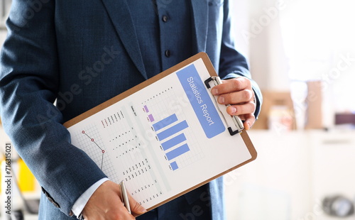Male arm in suit show stats graphic clipped to pad in office closeup. Stock exchange market advisor participation in negotiation study trade process white collar inspector check or explain money data