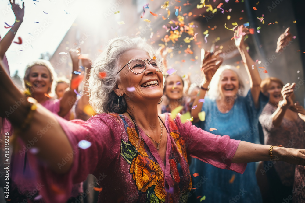 Happy senior woman dancing with confetti at a music festival. Group of friends having fun together. - obrazy, fototapety, plakaty 