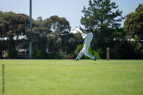 cricketer batting on a cricket pitch, a local cricket match being played on a green cricket oval in summer in australia