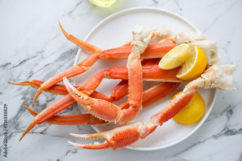 Plate with boiled crab claws and legs on a white marble background, horizontal shot, above view Plate with boiled crab claws and legs on a white marble background, horizontal shot, above view