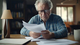 Elderly gentleman in glasses concentrating on reviewing papers, possibly related to personal finance or taxes.