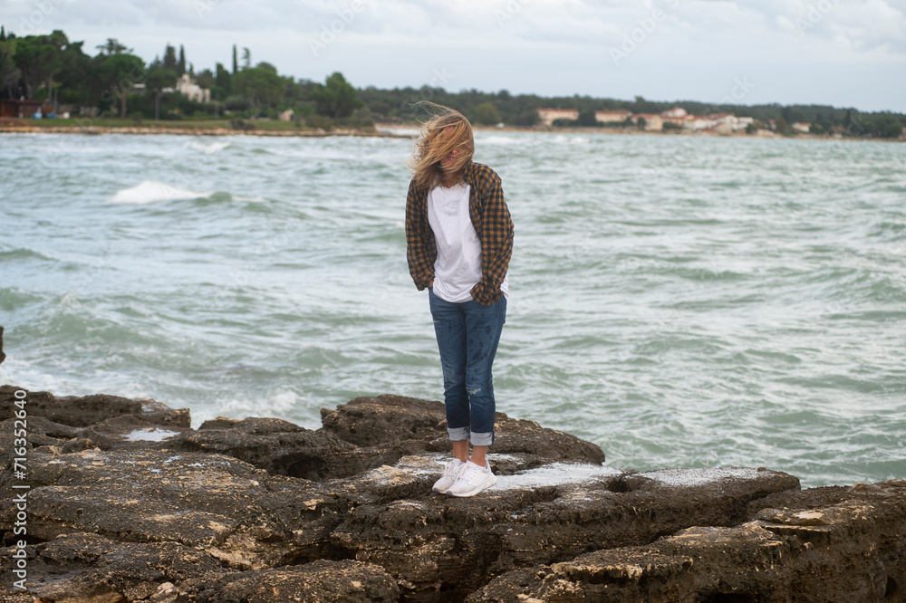 A woman stands on the coast of the Adriatic Sea in cold and windy weather