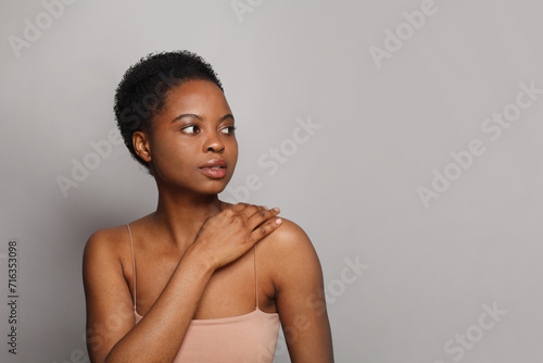 Charming healthy african american woman with clear fresh dark skin posing on gray background, fashion beauty portrait