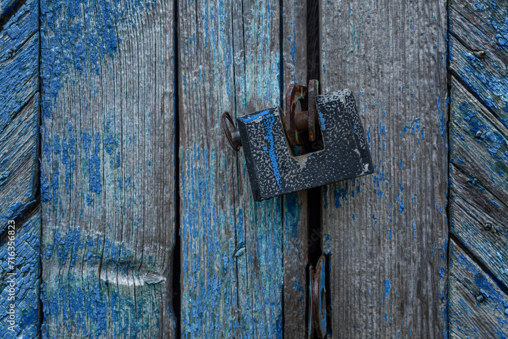An old padlock on a blue stripped wooden gate. Protect property and privacy. Close-up.