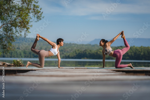 Athlete women, two female friends is doing yoga pose by the lake in the early morning, couple practicing exercise and training workout outdoor. Wellness and well being recreation, meditation balance.