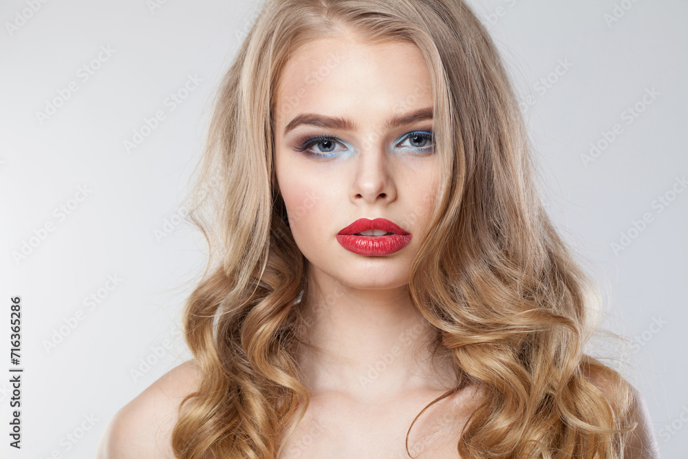 Fashionable young woman with clean fresh skin and long curly hair looking at camera on white studio wall background, portrait Fashionable young woman with clean fresh skin and long curly hair looking at camera on white studio wall background, portrait