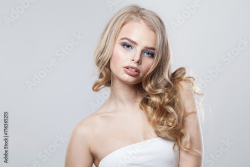 Elegant young woman with clean fresh skin and long curly hair looking at camera on white studio wall background, portrait