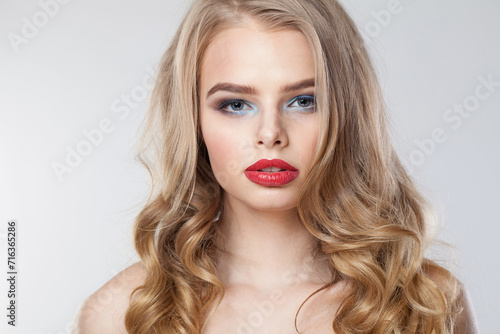 Fashionable young woman with clean fresh skin and long curly hair looking at camera on white studio wall background, portrait