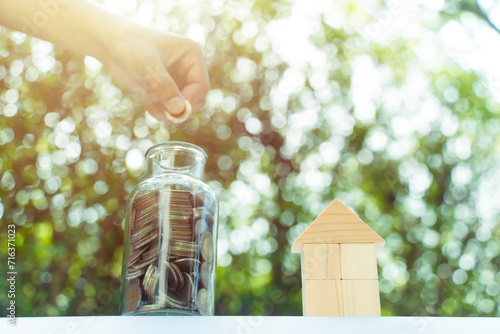 Saving money for house concept, Necessary cost for house, coin in bottle and wooden block house model. Money and financial for house concept. bokeh background in the public park, morning light.