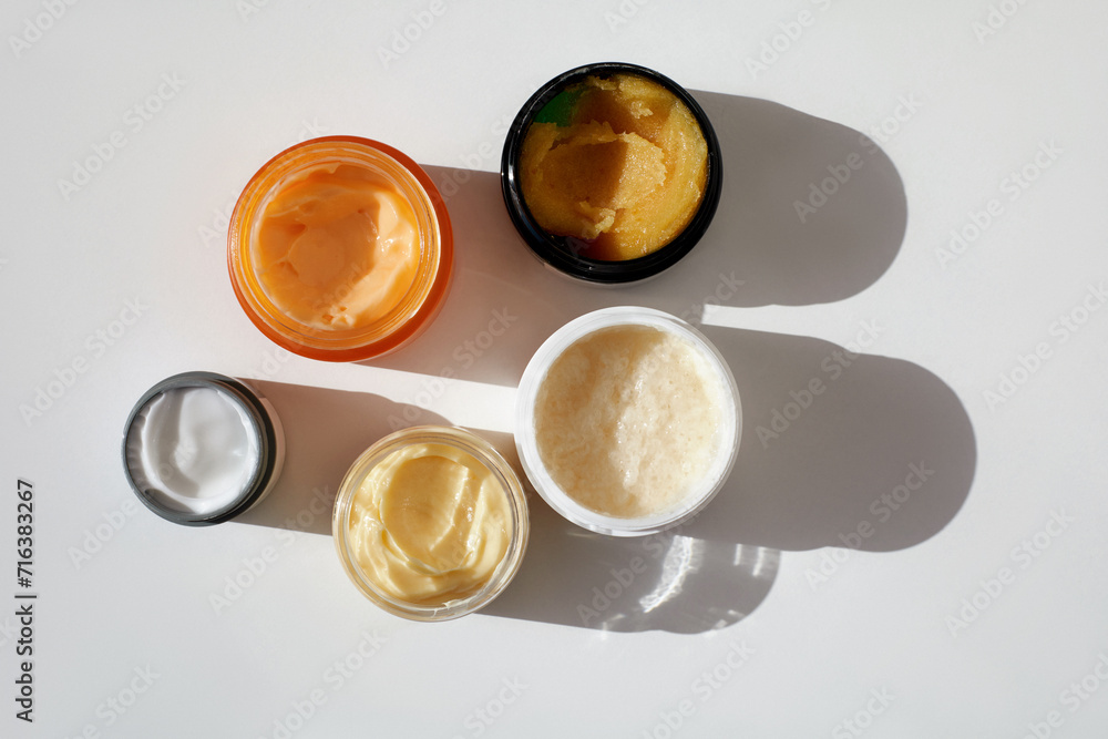 Different containers with natural herbal moisturising skin care products scrub, cream, peeling, green tea tree lotion and chea butter, top view, white background Different containers with natural herbal moisturising skin care products scrub, cream, peeling, green tea tree lotion and chea butter, top view, white background