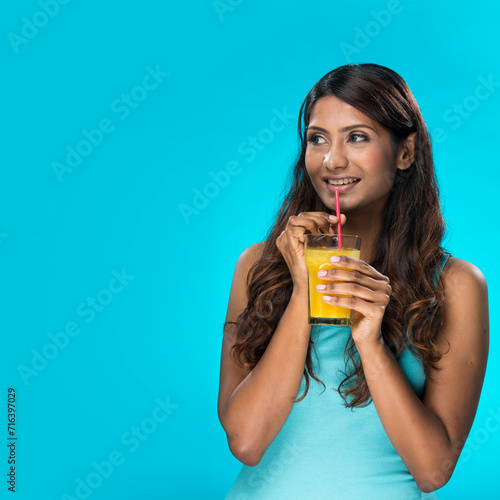 Indian woman drinking orange juice on blue background