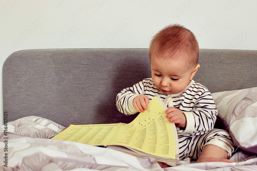 A cute little baby boy is carefully looking at a book with interest A cute little baby boy is carefully looking at a book with interest