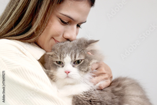 Cute white gray Persian cat comfortably in owner lap hands, happy fluffy pet comfortably being gently hugged with love feeling by owner. Adorable long hair kitty with woman owner relaxing at home.