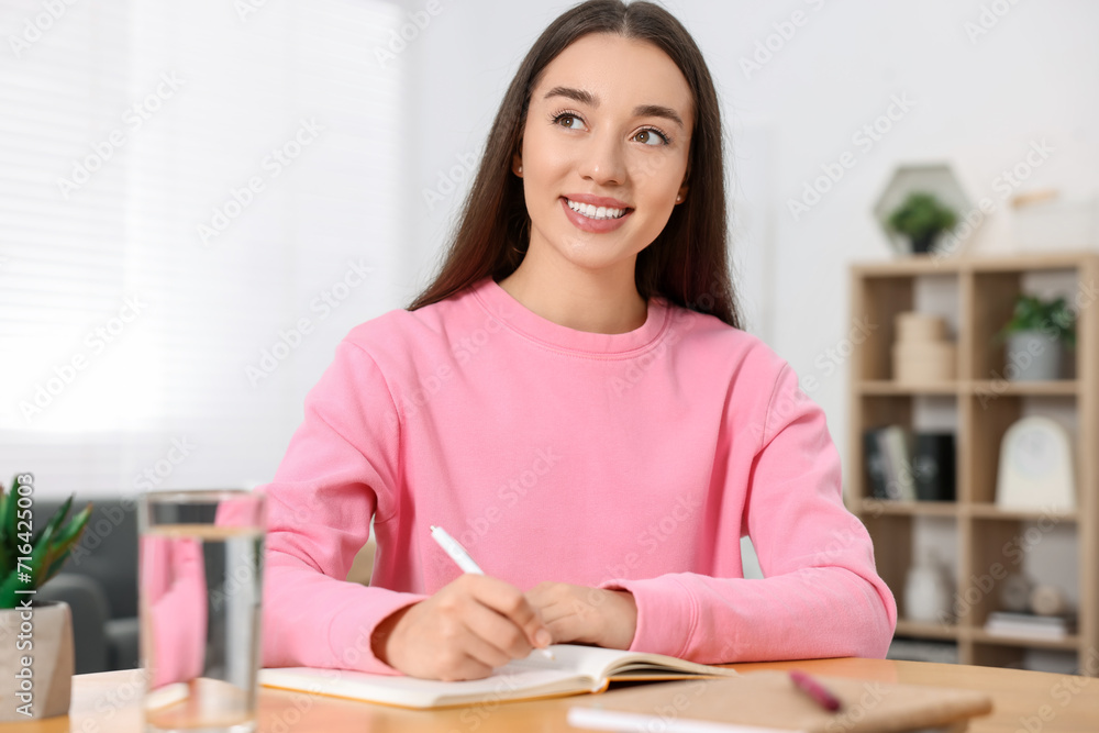 Young woman writing in notebook at wooden table indoors Young woman writing in notebook at wooden table indoors