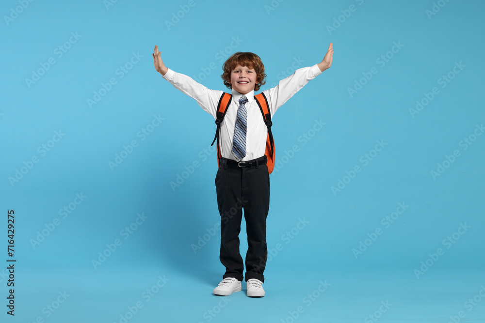 Happy schoolboy with backpack on light blue background Happy schoolboy with backpack on light blue background