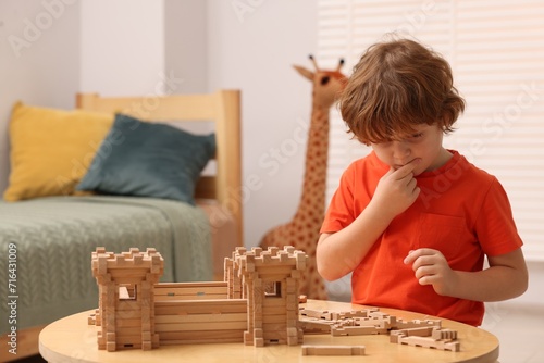 Little boy playing with wooden construction set at table in room. Child's toy