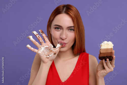 Young woman eating piece of tasty cake on purple background