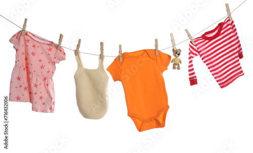 Different baby clothes and bear toy drying on laundry line against white background