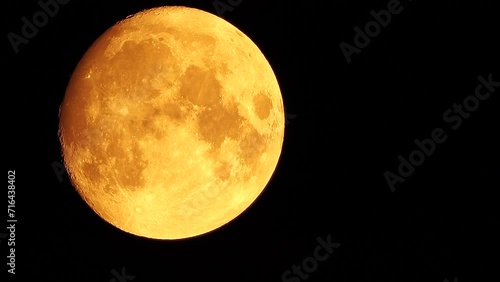 A glowing golden huge full moon seen from earth through the atmosphere against a starry night sky. A large full moon moves across the sky, the moon moving from the bottom left frame to the top right. photo
