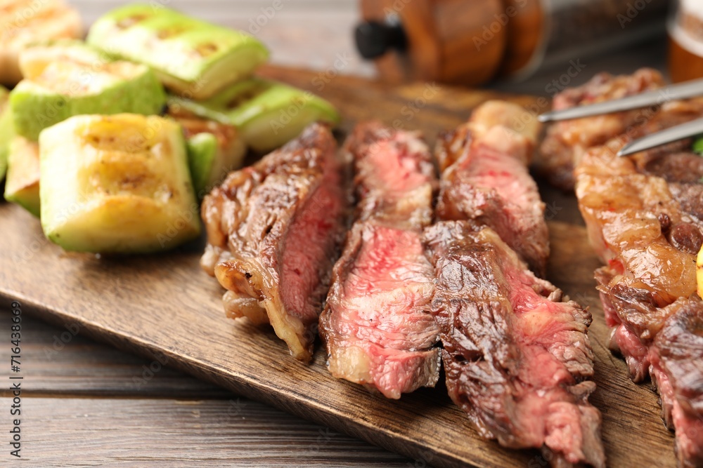 Delicious grilled beef steak and zucchini on wooden table, closeup