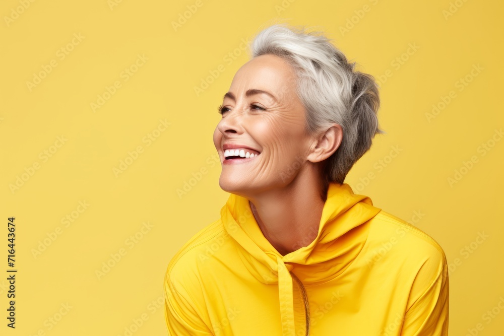 Mature woman in yellow hoodie smiling and looking up over yellow background. Mature woman in yellow hoodie smiling and looking up over yellow background.