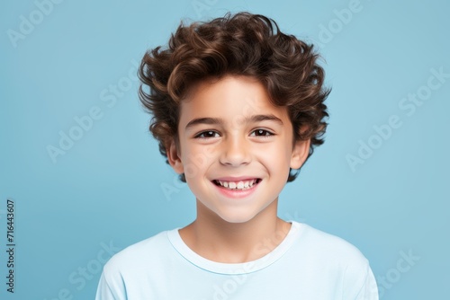closeup portrait of smiling little boy with curly hair over blue background.