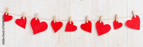 Red hearts on a rope with clothespins, on a white wooden background. Greeting card for Valentine's Day, banner.