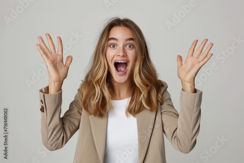 Photo studio shot of a stylish young businesswoman hand rise and yelling, looking very glad and surprised. The background is clean, solid white background.