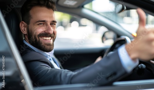 Side view of businessman in suit driving expensice car, smiling happily and showing thumb up, closeup. Young man entrepreneur going home by car after successful business meeting. © radekcho