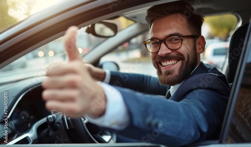 Side view of businessman in suit driving expensice car, smiling happily and showing thumb up, closeup. Young man entrepreneur going home by car after successful business meeting.