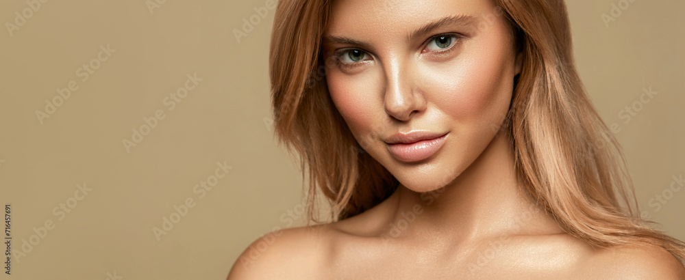 Naklejka premium A portrait of a woman with striking green eyes, glossy lips, and flowing blonde hair against a beige background, exuding elegance and natural beauty.