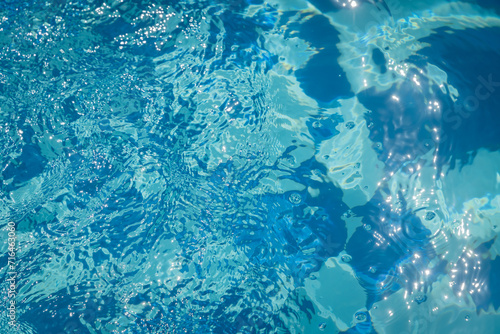 background with blue water surface of swimming pool with tiles and ripples in sun light photo
