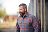 farmer wearing a plaid shirt, standing by an old wooden fence