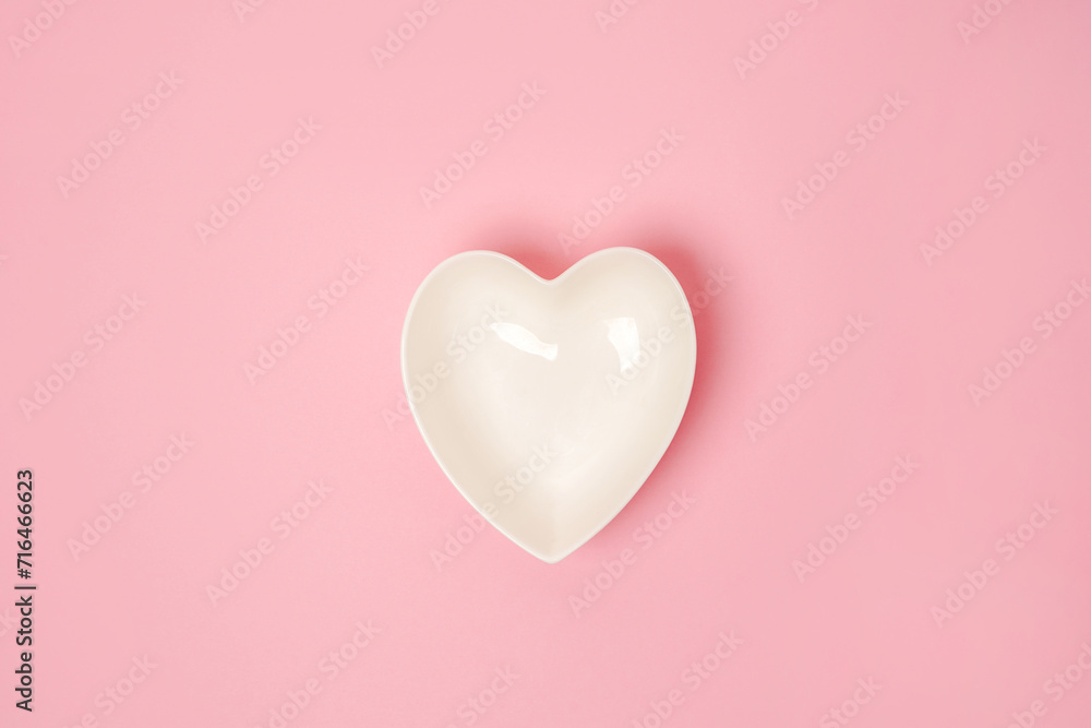 A white heart-shaped plate on pink background. The concept of love and happiness on Valentine's Day