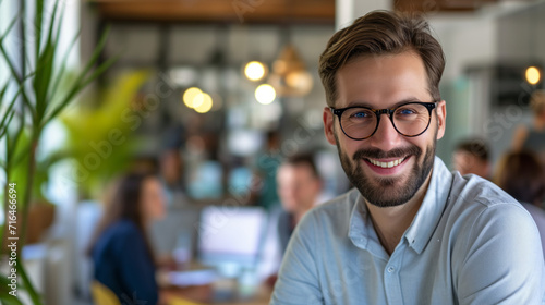 Smiling Businessman with Glasses in Office. Friendly young businessman wearing glasses smiling confidently in a modern collaborative office space.
