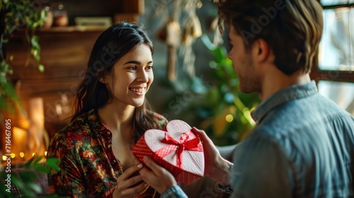 Young man is giving a present to his lovely girlfriend while they are sitting on couch at home