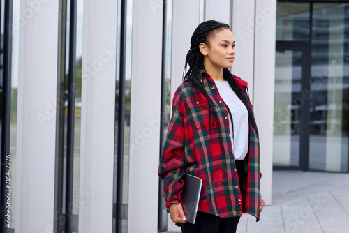 A student with a laptop on the background of buildings. African-American woman with good academic performance at university.